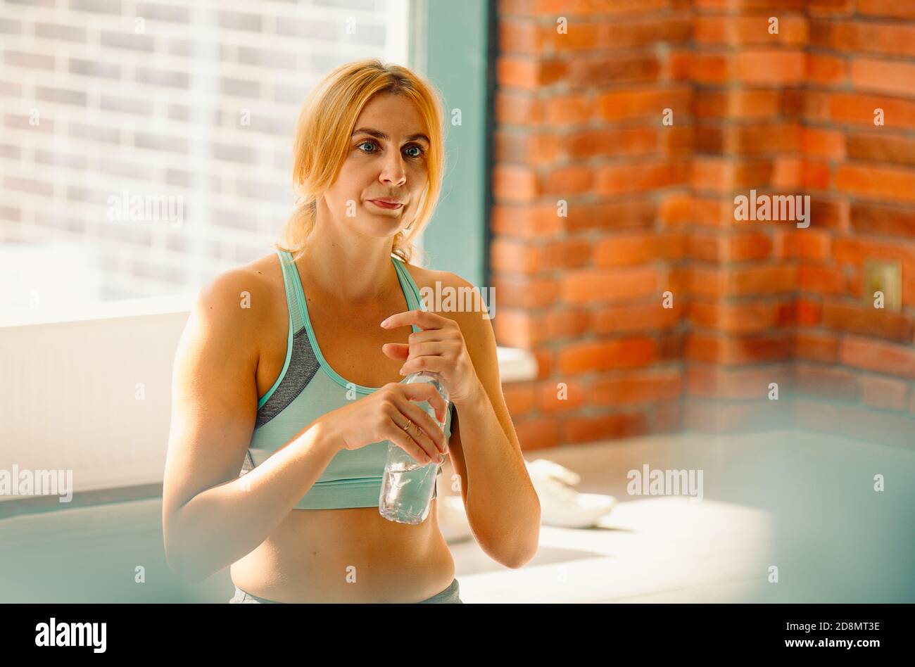 Belle jeune femme tenant une bouteille d'eau après l'entraînement dans la salle de gym. Photo avec espace latéral vide Banque D'Images