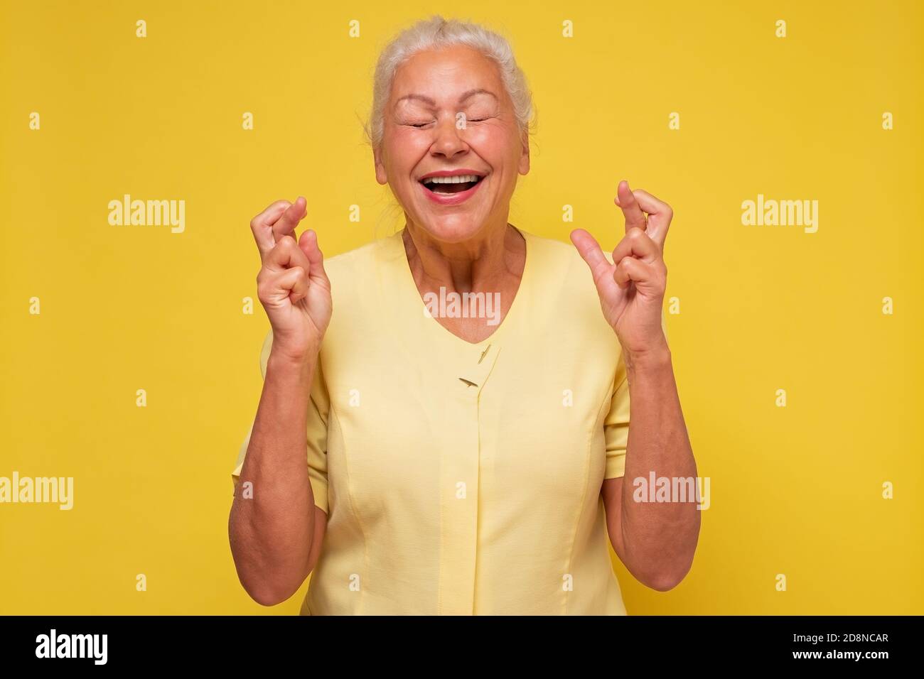 Femme âgée ayant un look excité, superstititieux et naïf, en gardant les doigts croisés, Banque D'Images