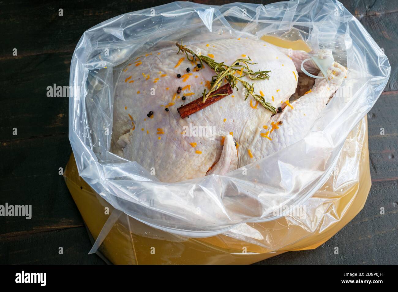 Saupoudrer une dinde dans un sac en plastique : une dinde crue dans de la saumure bourbon avec du romarin, des bâtonnets de cannelle, des grains de poivre noir et du zeste d'orange Banque D'Images