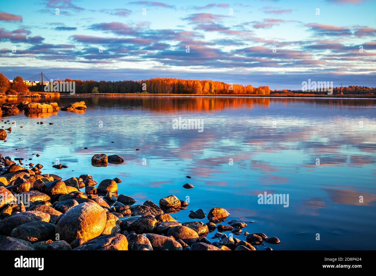 Ciel coloré avec des nuages roses et bleus reflétés dans une surface d'eau calme au lever du soleil. Côte de baie avec ville et orangers. Paysage du matin d'automne Banque D'Images