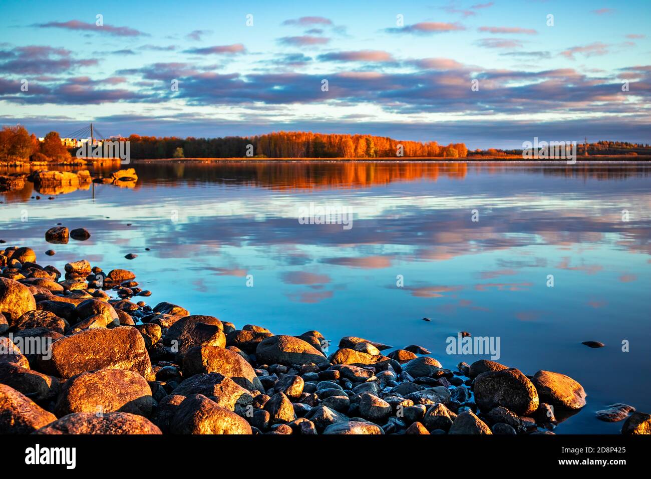 Les pierres brillent en plein soleil le matin sur une plage du lac. Ciel bleu avec des nuages colorés reflétés dans une surface d'eau calme au coucher du soleil. Paysage de la soirée d'automne. Banque D'Images