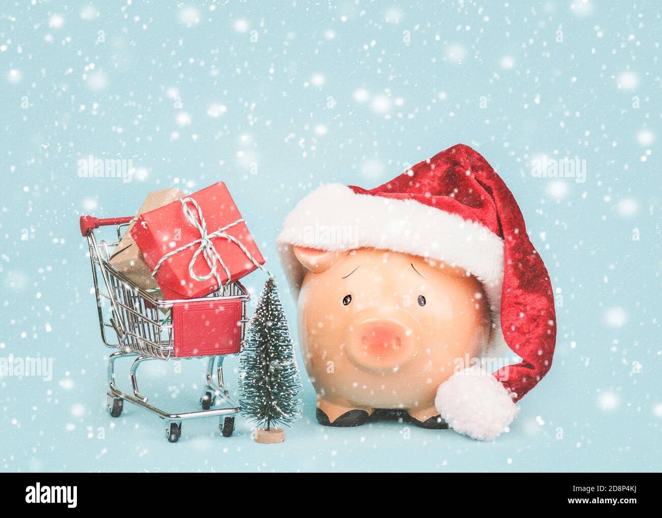 Arrière-plan du concept de Noël. Tirelire avec chapeau de père Noël et panier avec cadeaux de noël sur fond bleu Banque D'Images