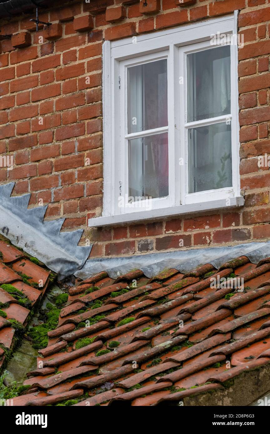 fenêtre et toit en tuiles sur un cottage de campagne d'époque avec de la mousse poussant dans la gouttière causant un blocage de plomb clignotant sur le toit en tuiles Banque D'Images