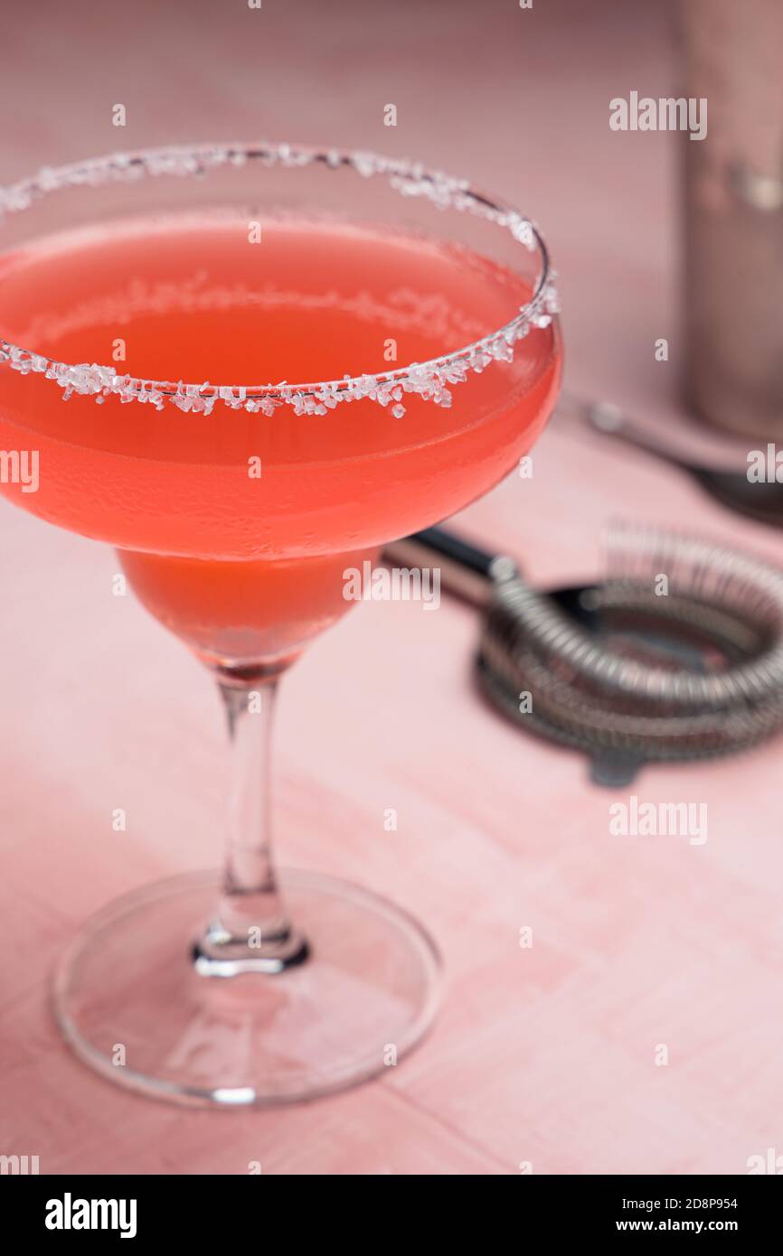 Cocktail de Margarita rouge et quelques accessoires de barman sur un rose arrière-plan Banque D'Images