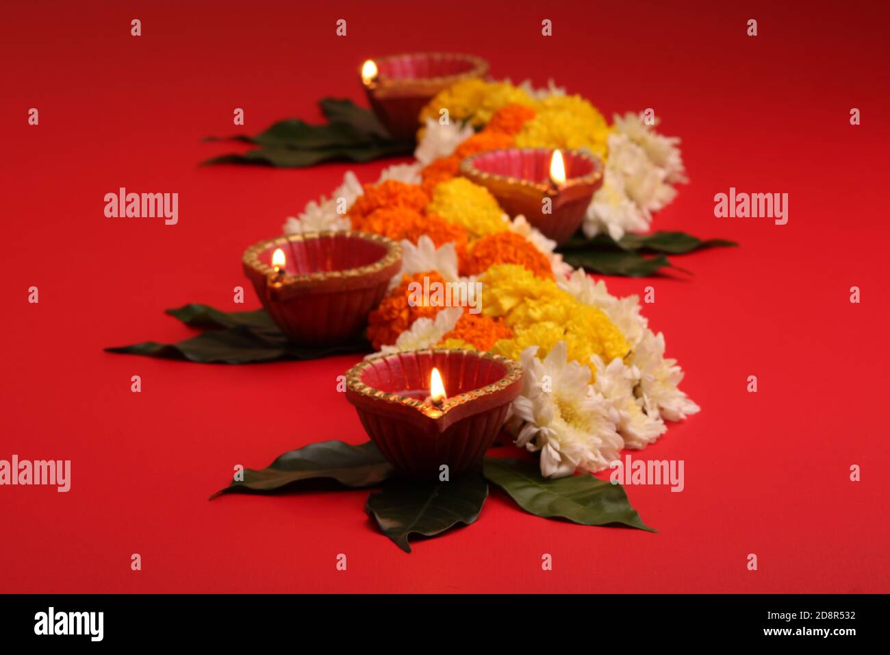 Fleur Rangoli pour Diwali ou Pongal Festival fait à l'aide de fleurs Marigold ou Zendu et de la lampe à huile de Clay sur fond rouge. Espace de copie. Lumière sur le côté gauche Banque D'Images