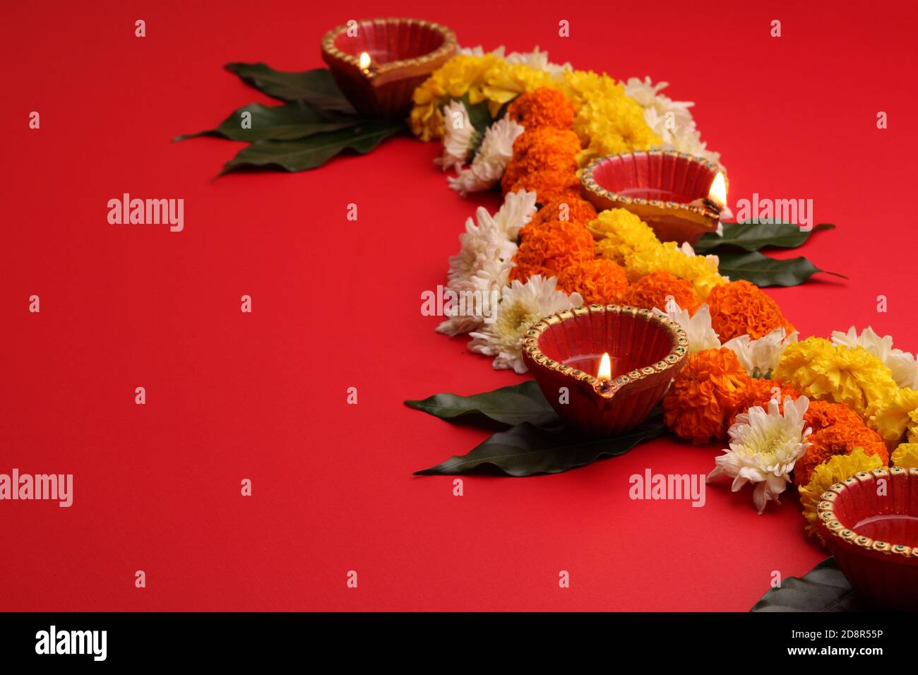 Fleur Rangoli pour Diwali ou Pongal Festival fait à l'aide de fleurs Marigold ou Zendu et de la lampe à huile de Clay sur fond rouge. Espace de copie. Lumière sur le côté gauche Banque D'Images