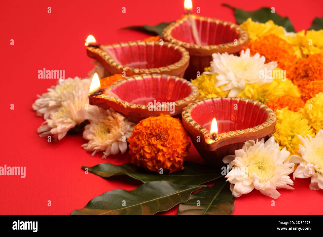 Fleur Rangoli pour Diwali ou Pongal Festival fait à l'aide de fleurs Marigold ou Zendu et de la lampe à huile de Clay sur fond rouge. Espace de copie. Lumière sur le côté gauche Banque D'Images