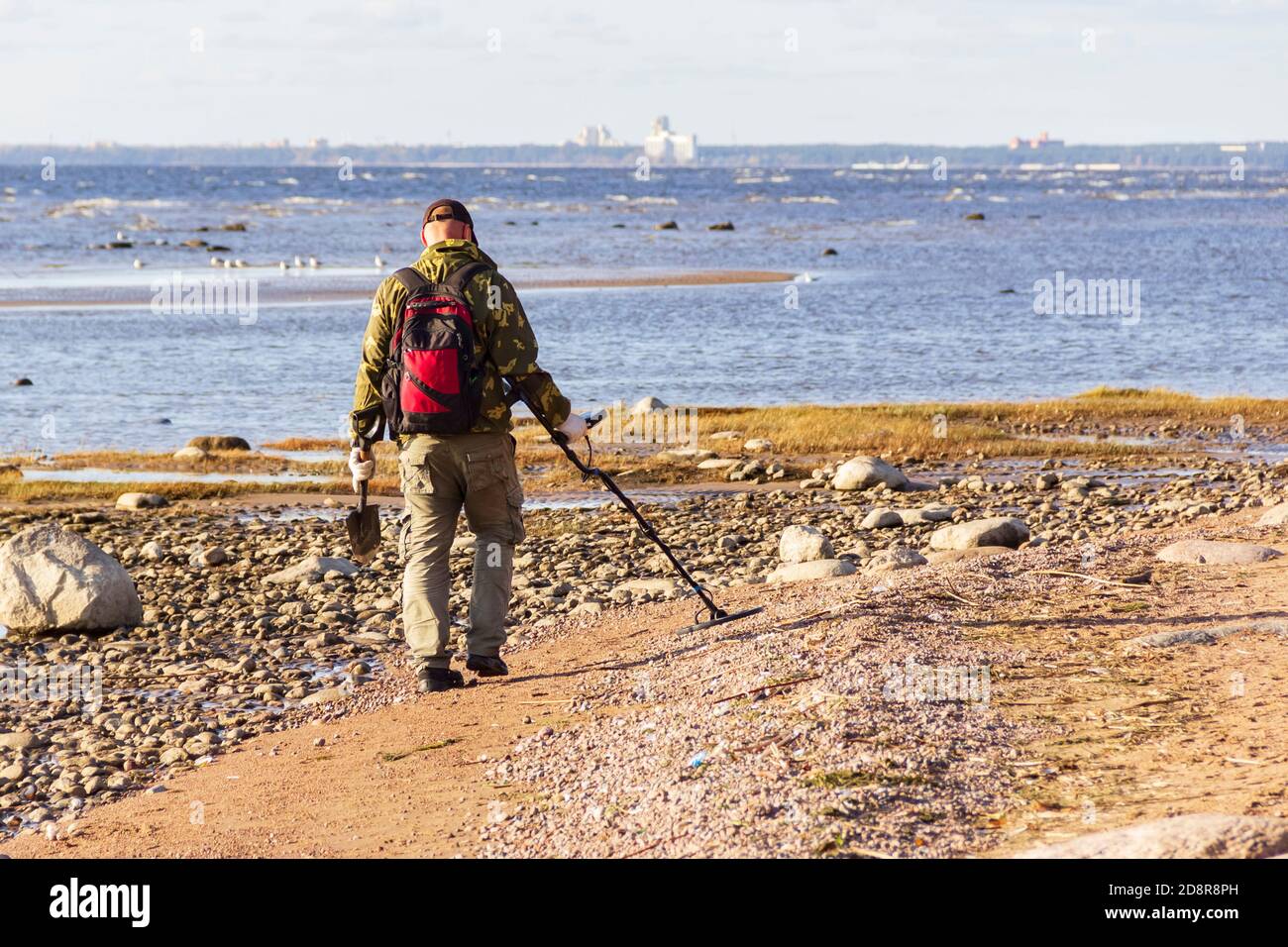 Un chasseur de trésors avec un détecteur de métal marche le long de la plage de sable déserte à la recherche de pièces de monnaie perdues et de bijoux. Banque D'Images