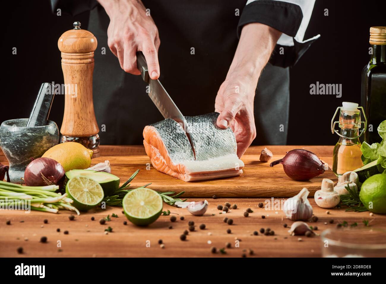 Le chef coupe le filet de saumon dans des steaks sur une planche de bois Banque D'Images