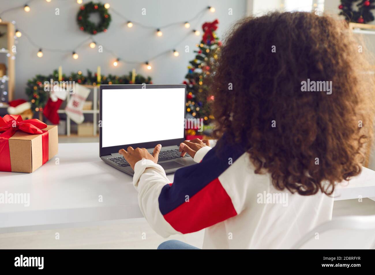 Jeune fille maurique assise à une table devant un ordinateur portable dans une pièce avec des décorations de Noël. Banque D'Images