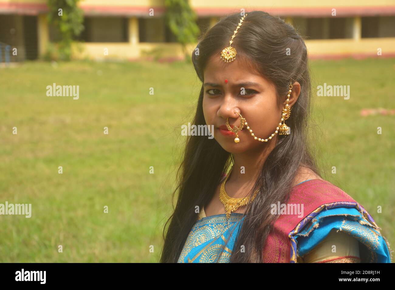 Gros plan d'une adolescente bengali indienne avec de longs poils foncés portant un anneau de nez traditionnel sari et des bijoux, boucles d'oreilles, collier et tika de maang Banque D'Images