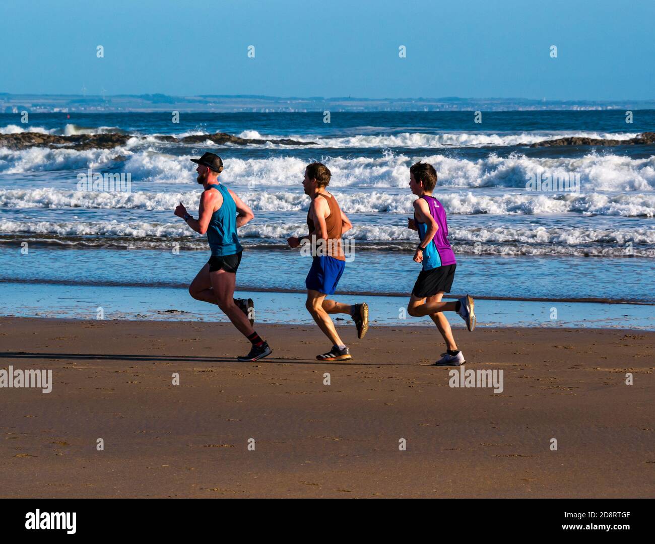 Trio de coureurs en course à pied sur Broadsands Beach par beau temps, avec des avant-premières se brisant sur la côte, East Lothian, Écosse, Royaume-Uni Banque D'Images