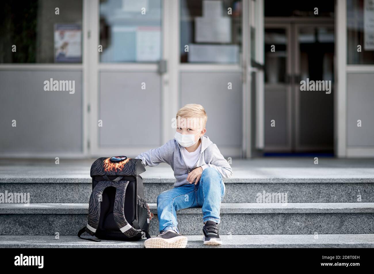 Enfant avec masque de visage assis sur les marches du école Banque D'Images