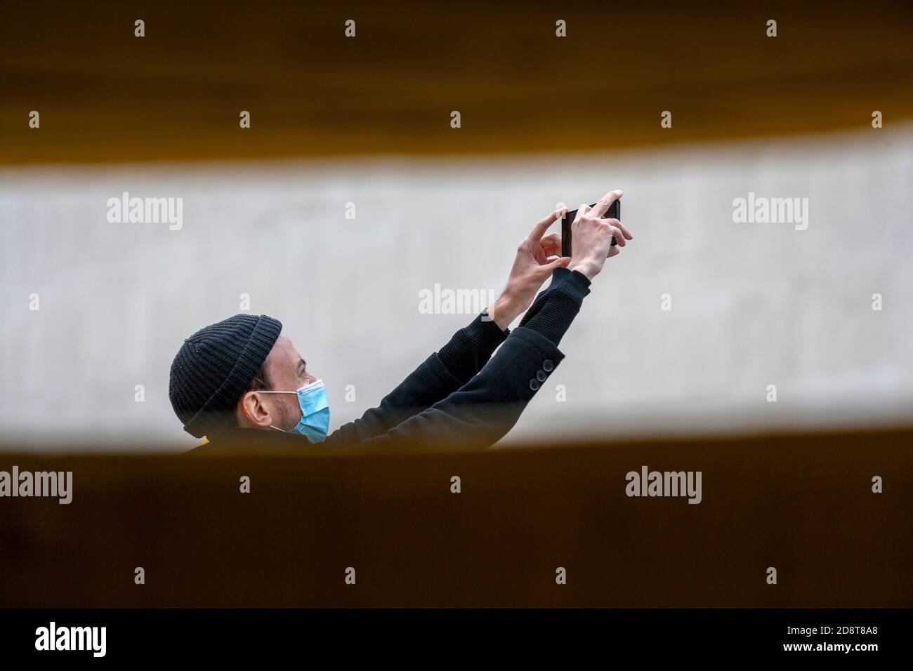 Homme, portant un bonnet beanie et un masque facial, utilisant son téléphone mobile pour faire une vidéo numérique. Southbank de Londres, Royaume-Uni Banque D'Images