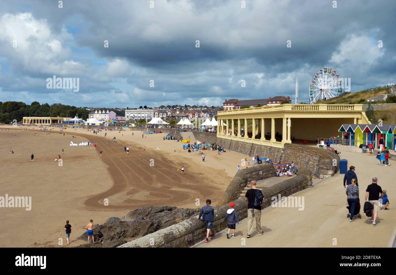 Barry Island, pays de Galles - 6 août 2017 : personnes marchant le long de la promenade avec les pistes d'un tracteur de nettoyage visible sur la plage visible Banque D'Images