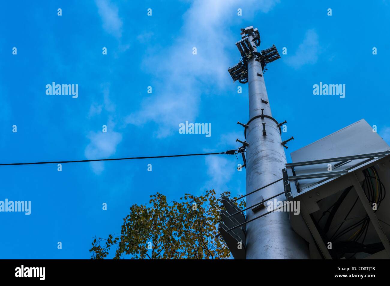 Tour cellulaire contre le ciel bleu avec des nuages moelleux et arbres avec fils Banque D'Images