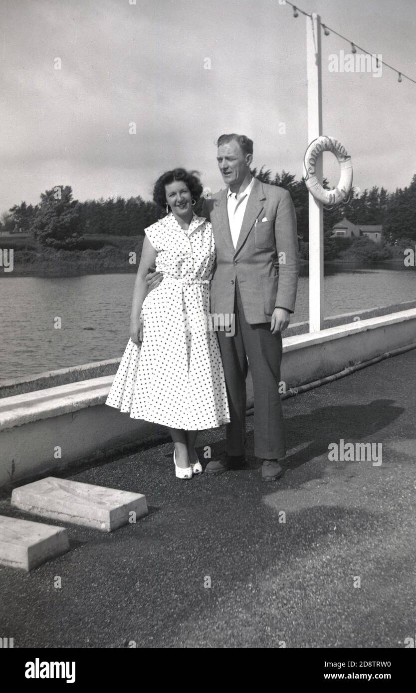 1950s, historique, homme et femme debout sur une jetée à l'île de Haiing, Hampshire, Angleterre, Royaume-Uni, la femme portant des chaussures blanches et une robe à pois, un style féminin populaire et à la mode à cette époque. Banque D'Images