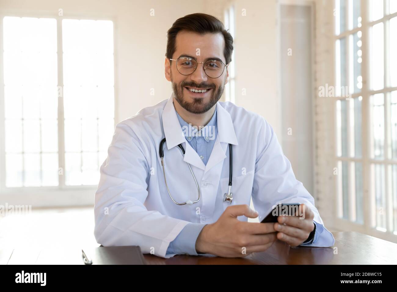 Médecin confiant assis à un bureau avec un téléphone capable de vous aider Banque D'Images