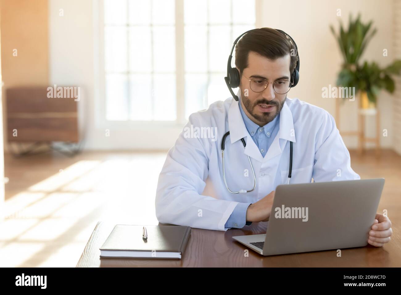 Jeune médecin consultant attentif concentré assis à l'ordinateur portable dans le micro-casque Banque D'Images