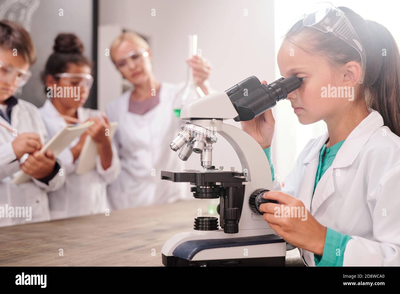 Une écolière intelligente et sérieuse en whitecavoine regardant au microscope en chimie leçon Banque D'Images