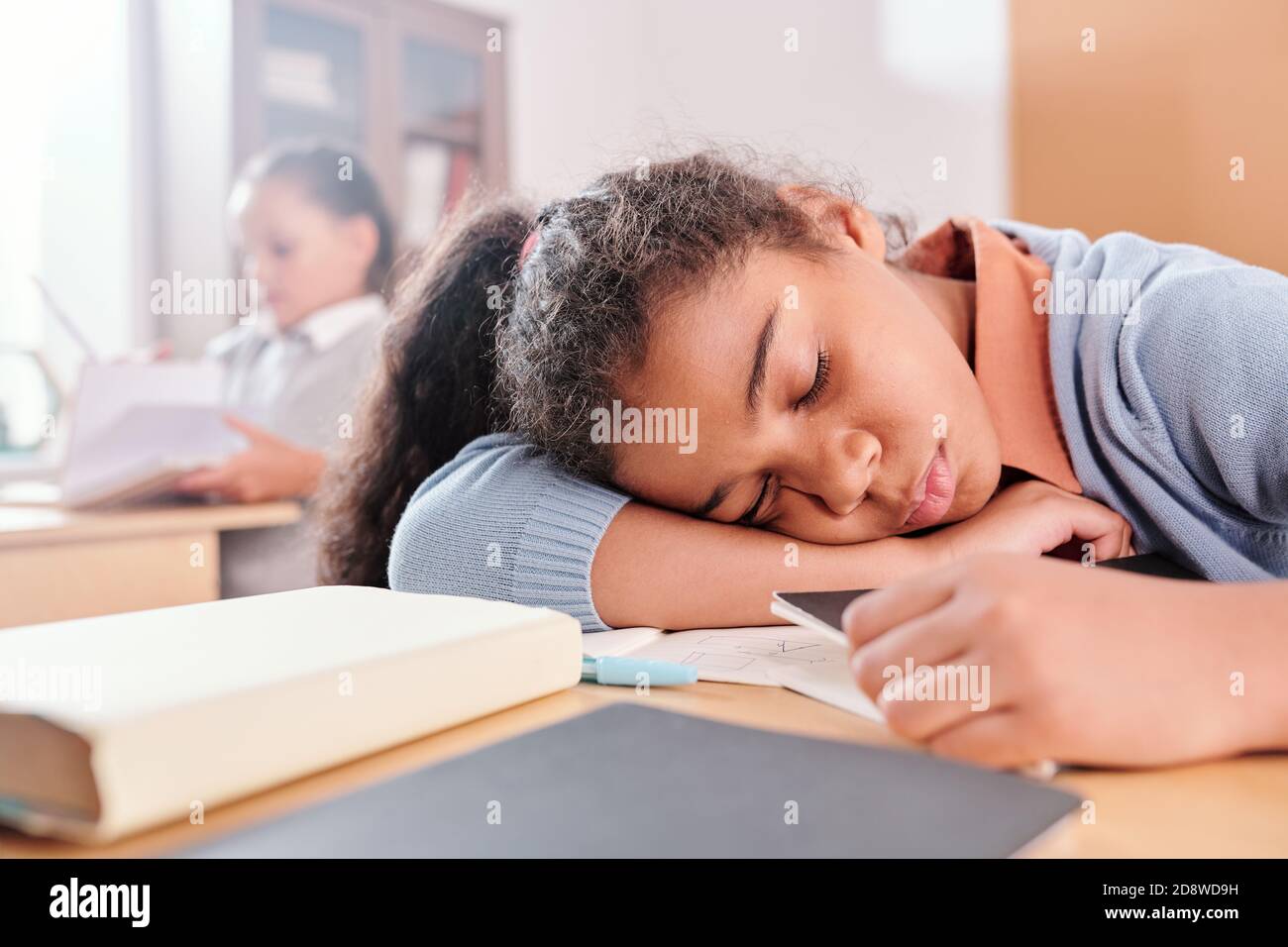 Une écolière épuisée ou lasse en vêtements décontractés qui tient la tête sur le bureau pendant le rodage Banque D'Images