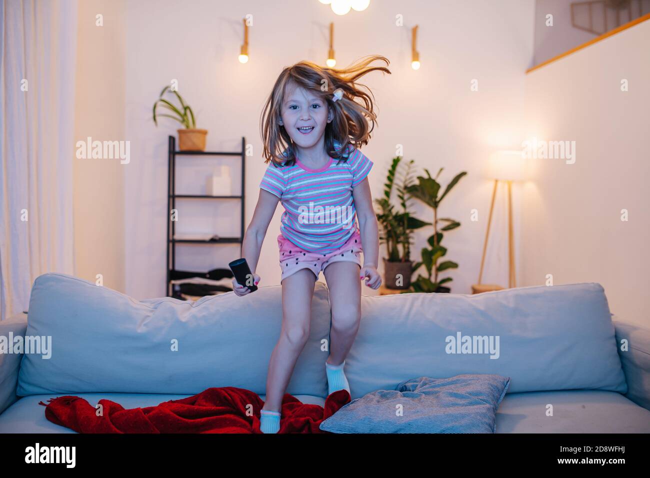 Une petite fille sautant du canapé devant la télévision avec télécommande à portée de main Banque D'Images