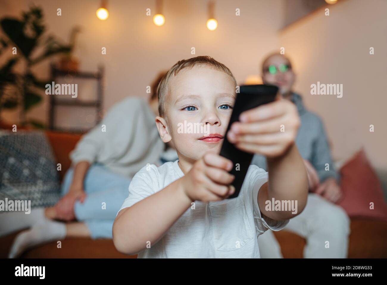 Mignon petit garçon est de changer de téléviseur avec une télécommande dans une pièce sombre éclairé. Banque D'Images