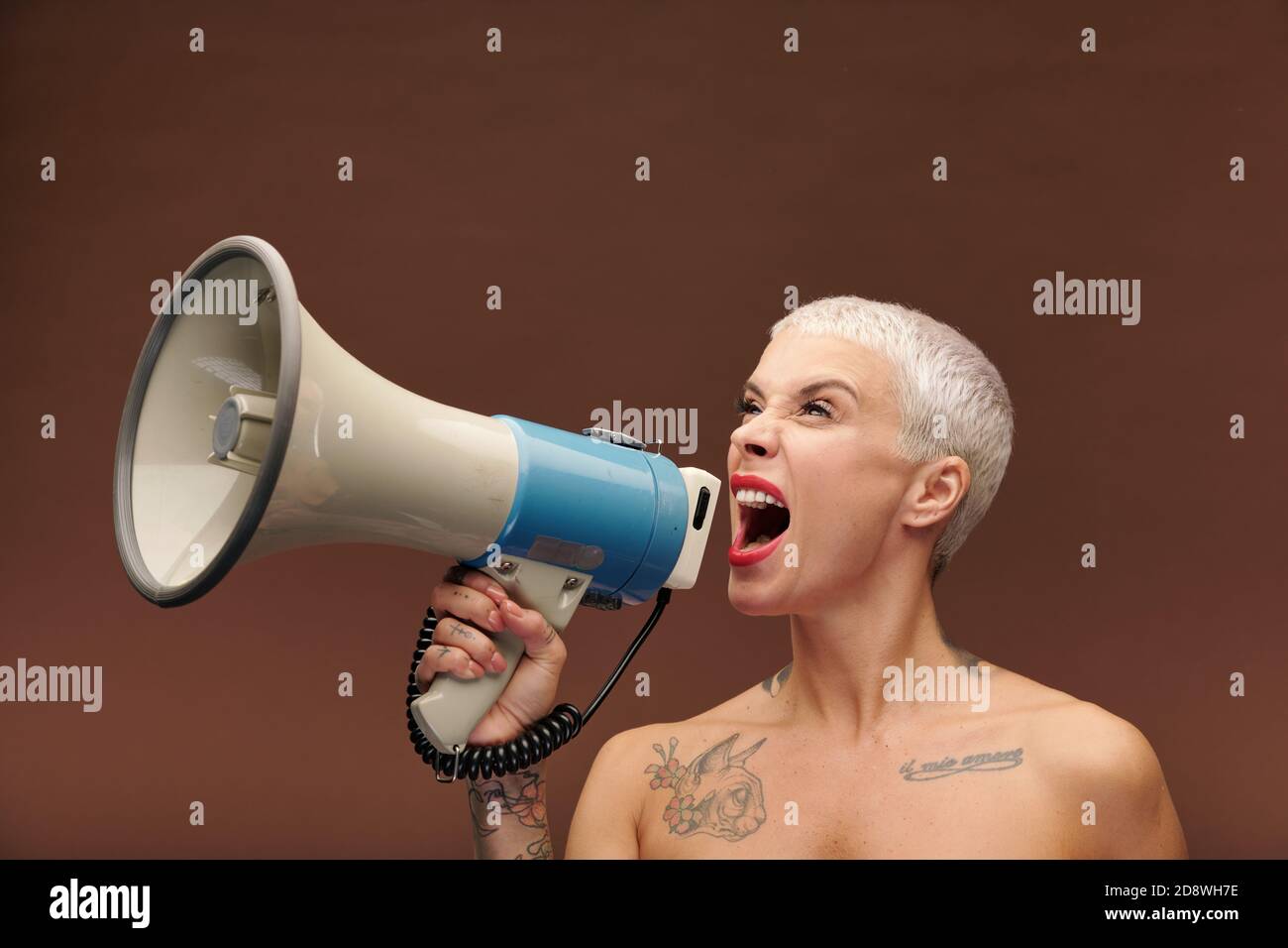 Femelle très en colère avec des tatouages sur le bras, la poitrine et le cou criant en mégaphone Banque D'Images