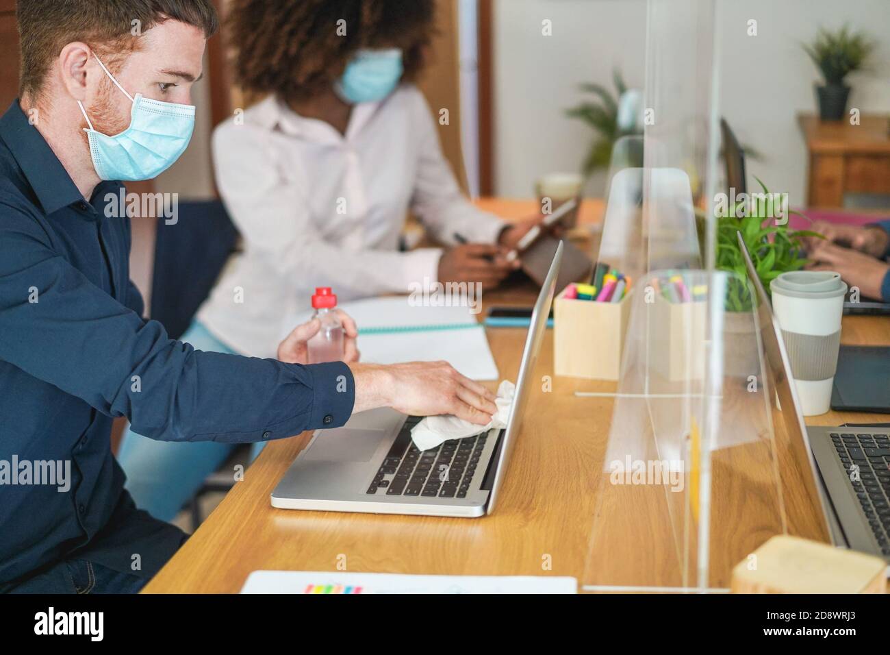 Jeune travailleur utilisant du gel désinfectant pour désinfecter son ordinateur portable Dans le bureau de travail de collègue - concentrez-vous sur l'œil de l'homme Banque D'Images