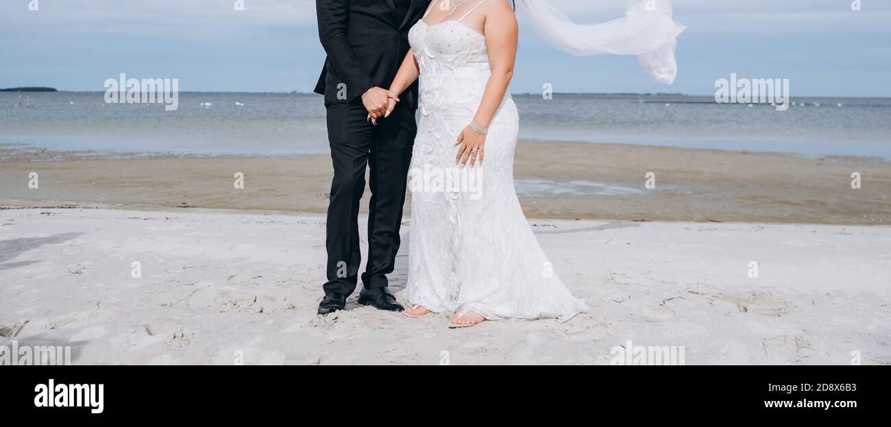 Couple de mariage dansant à la plage, la jeune mariée porte une robe blanche et un long voile. Banque D'Images