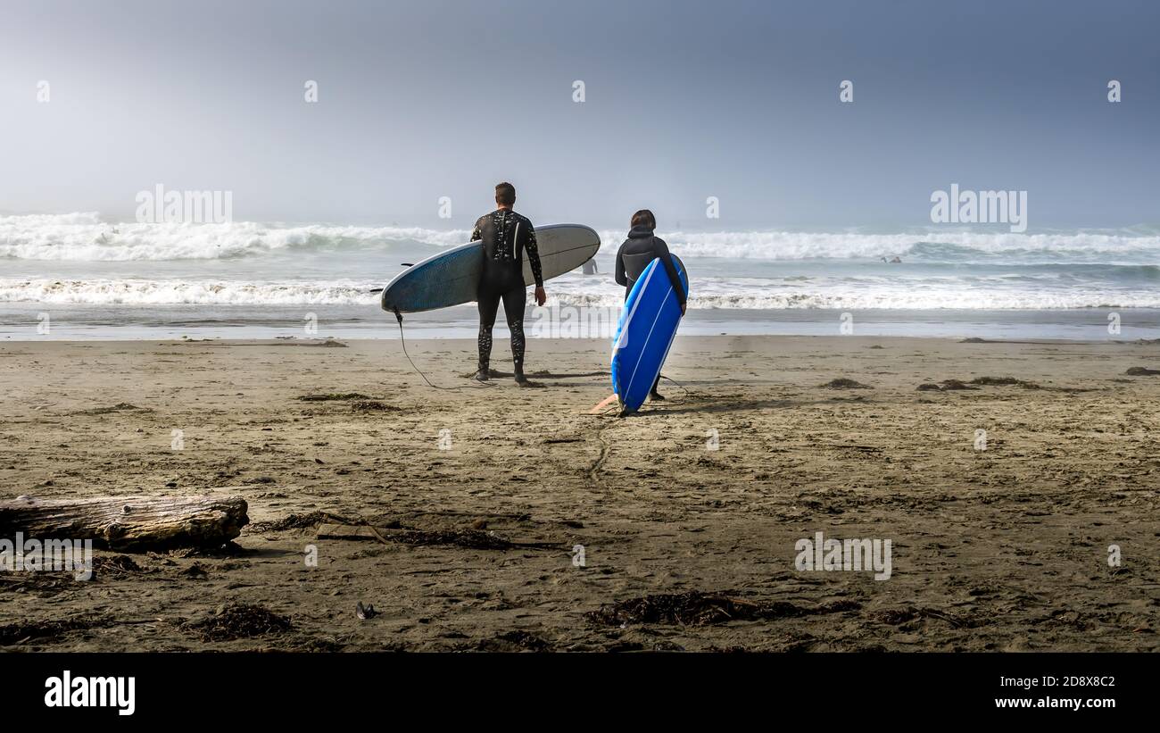 Deux surfeurs se dirigeant vers l'océan Pacifique couvert de brume à Cox Bay Beach, au parc national Pacific Rim, sur l'île de Vancouver, Colombie-Britannique, Canada Banque D'Images