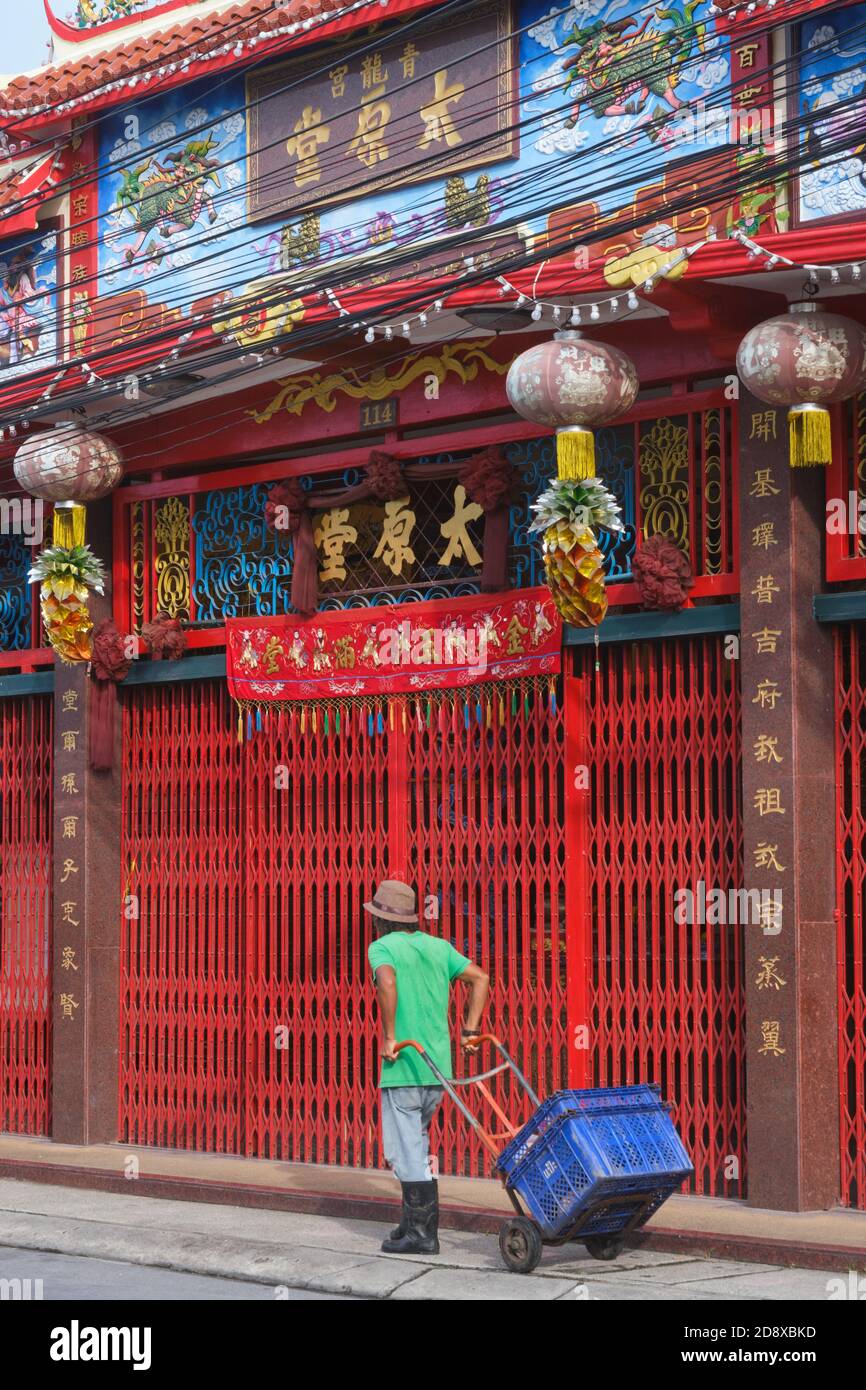 Un portier avec chariot à main passant devant le sanctuaire Thye Guan Thong, un temple construit par des immigrants chinois dans la vieille ville de Phuket, Phuket, Thaïlande Banque D'Images