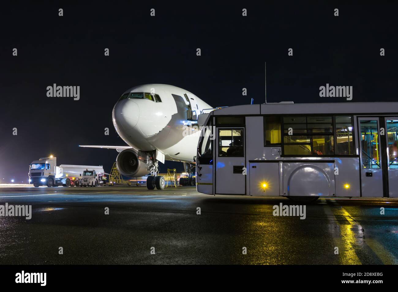 Avion passager à gros corps blanc et navette aéroport sur le tablier de nuit. Manutention au sol de l'avion Banque D'Images