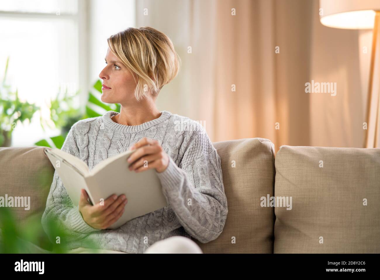 Portrait d'une femme se détendant avec un livre à l'intérieur à la maison, concept de soins de santé mentale. Banque D'Images