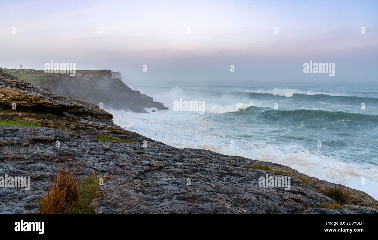D'énormes vagues de tempête se sont écrasues sur le Cap Ajo en Espagne avec le phare sur les falaises au-dessus au lever du soleil Banque D'Images
