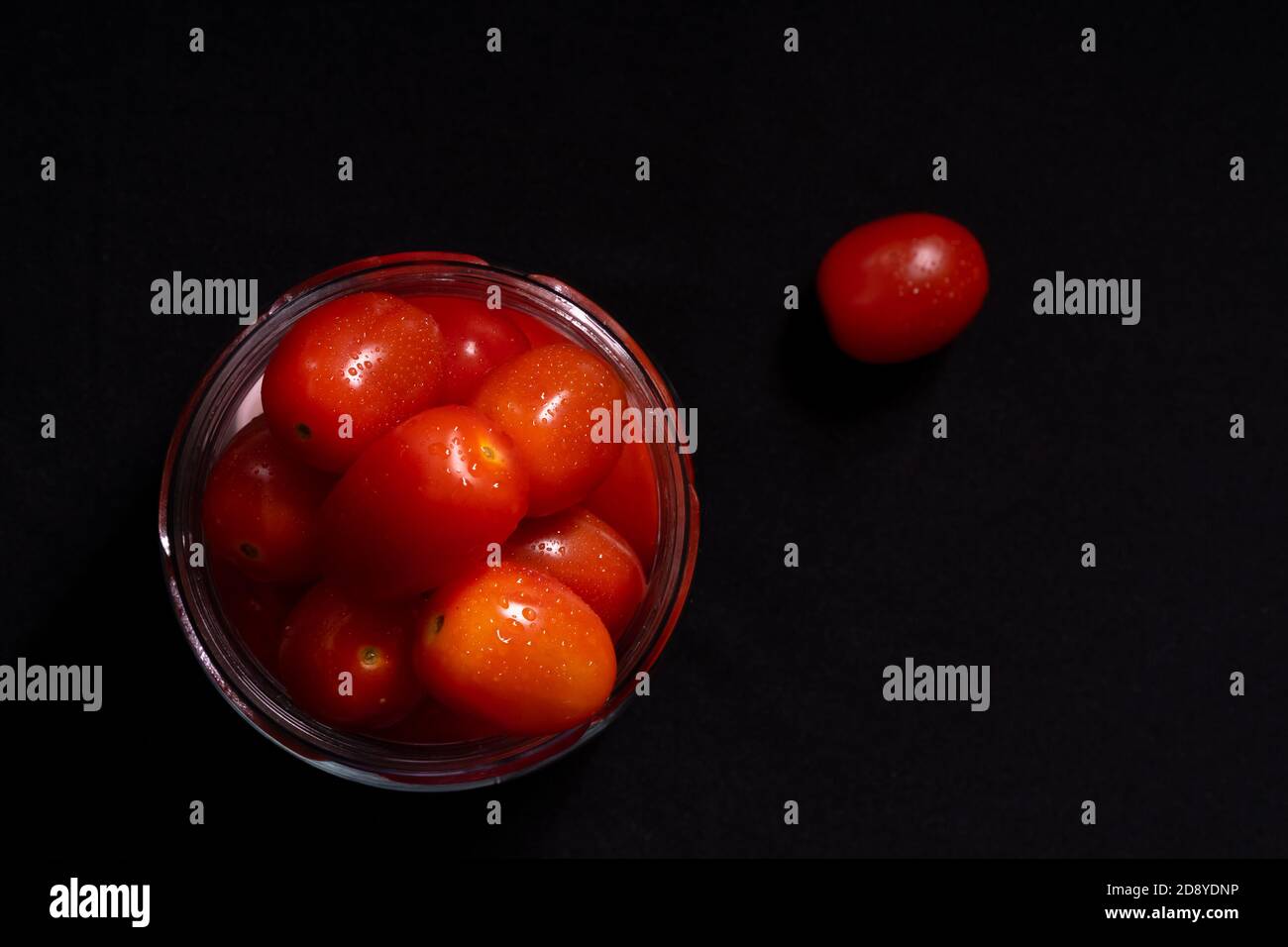 Photo clé basse de tomates cerises fraîches dans un pot en verre. Photo foncée de tomates cerises dans un pot en verre isolé sur fond noir. Banque D'Images