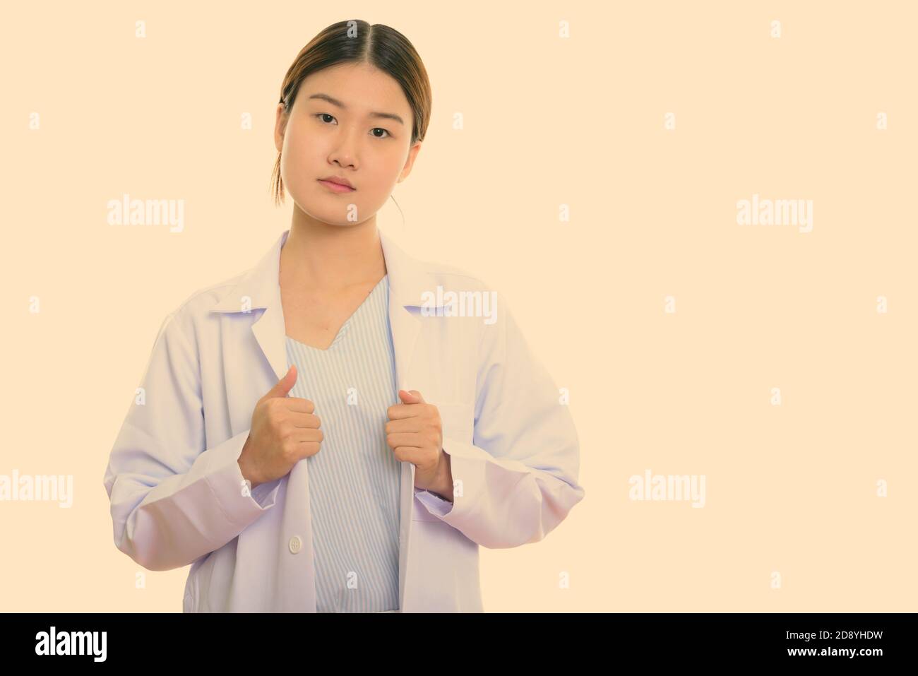 Photo de studio de jeune femme asiatique belle médecin tenant un manteau de laboratoire avec les deux mains Banque D'Images