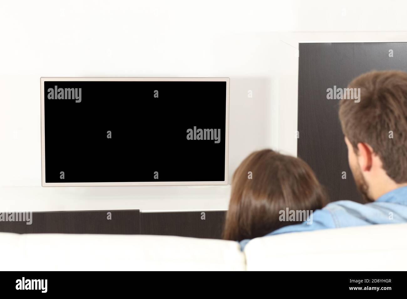 Vue arrière d'un couple en train de regarder la télévision avec blanc écran assis dans le canapé à la maison Banque D'Images