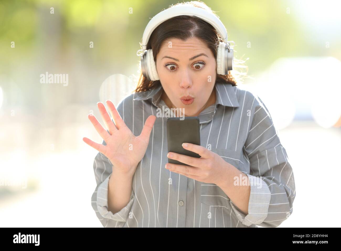 Vue avant portrait d'une femme stupéfaite portant un casque de trouver musique sur smartphone Banque D'Images