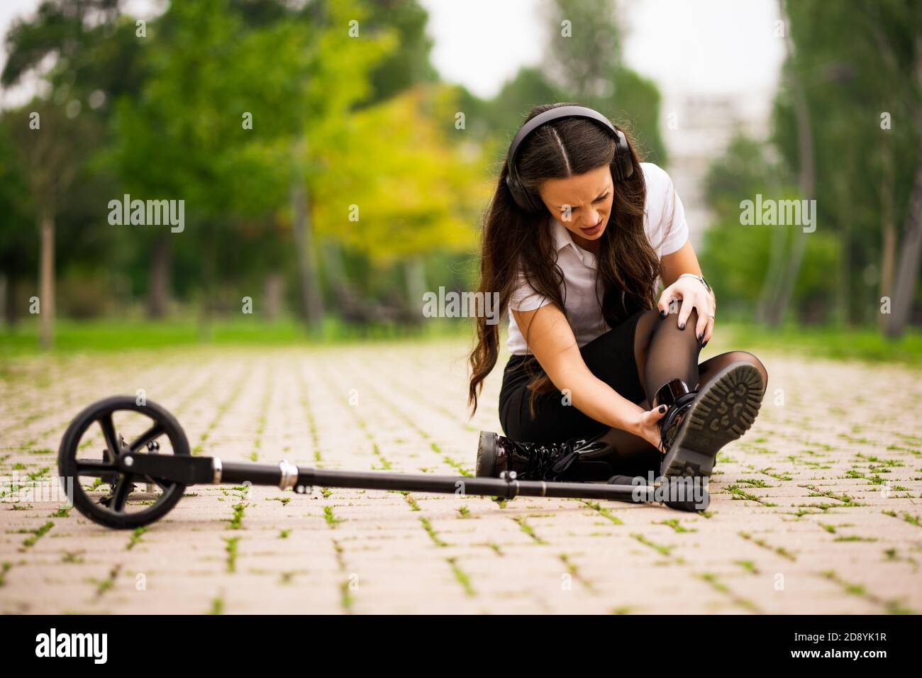 Femme d'affaires est en scooter de poussée dans le parc. Elle est tombée et tordue sa cheville. Banque D'Images