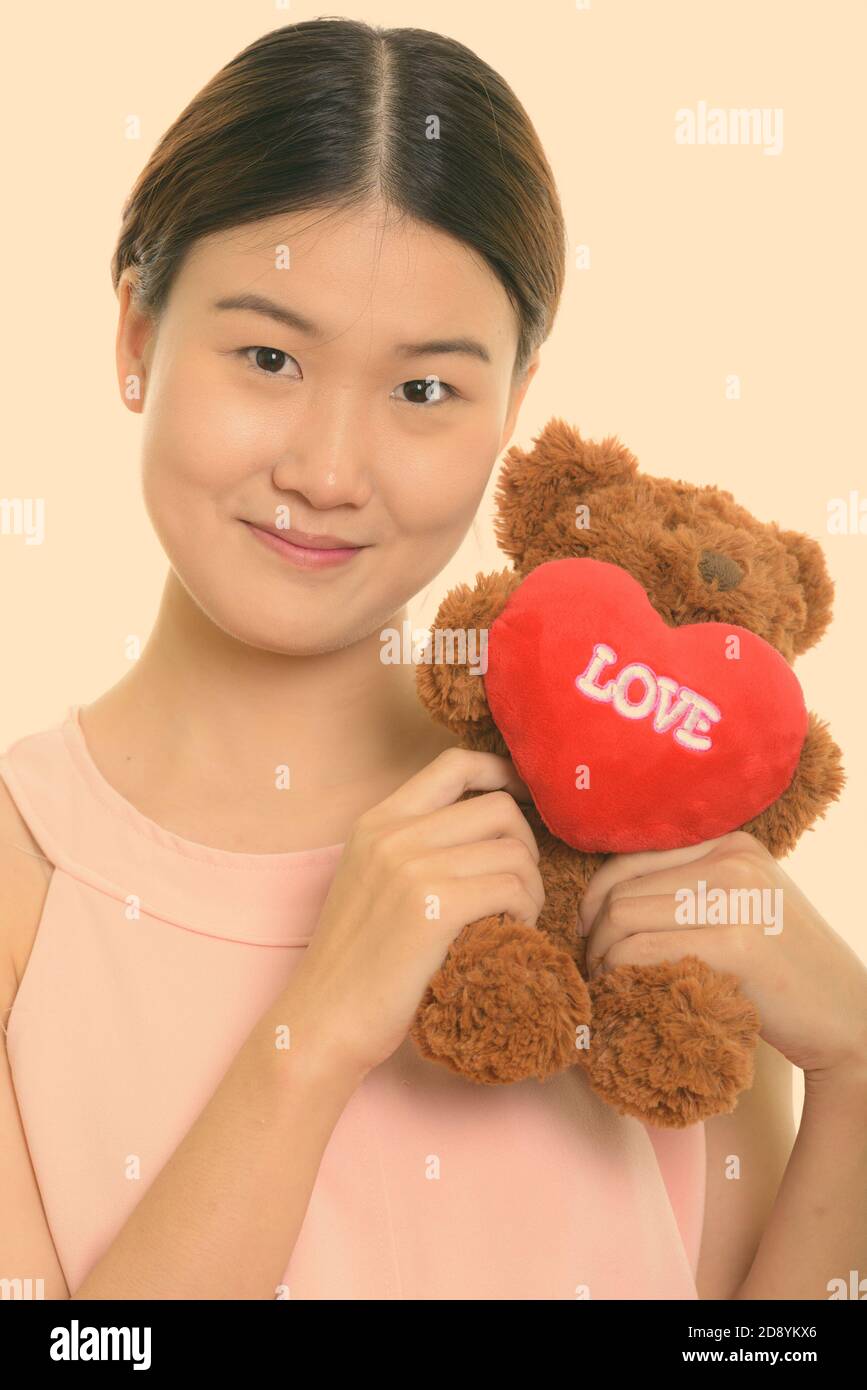 Gros plan de la jeune femme asiatique belle tenant l'ours en peluche avec le coeur et le signe d'amour près du visage Banque D'Images