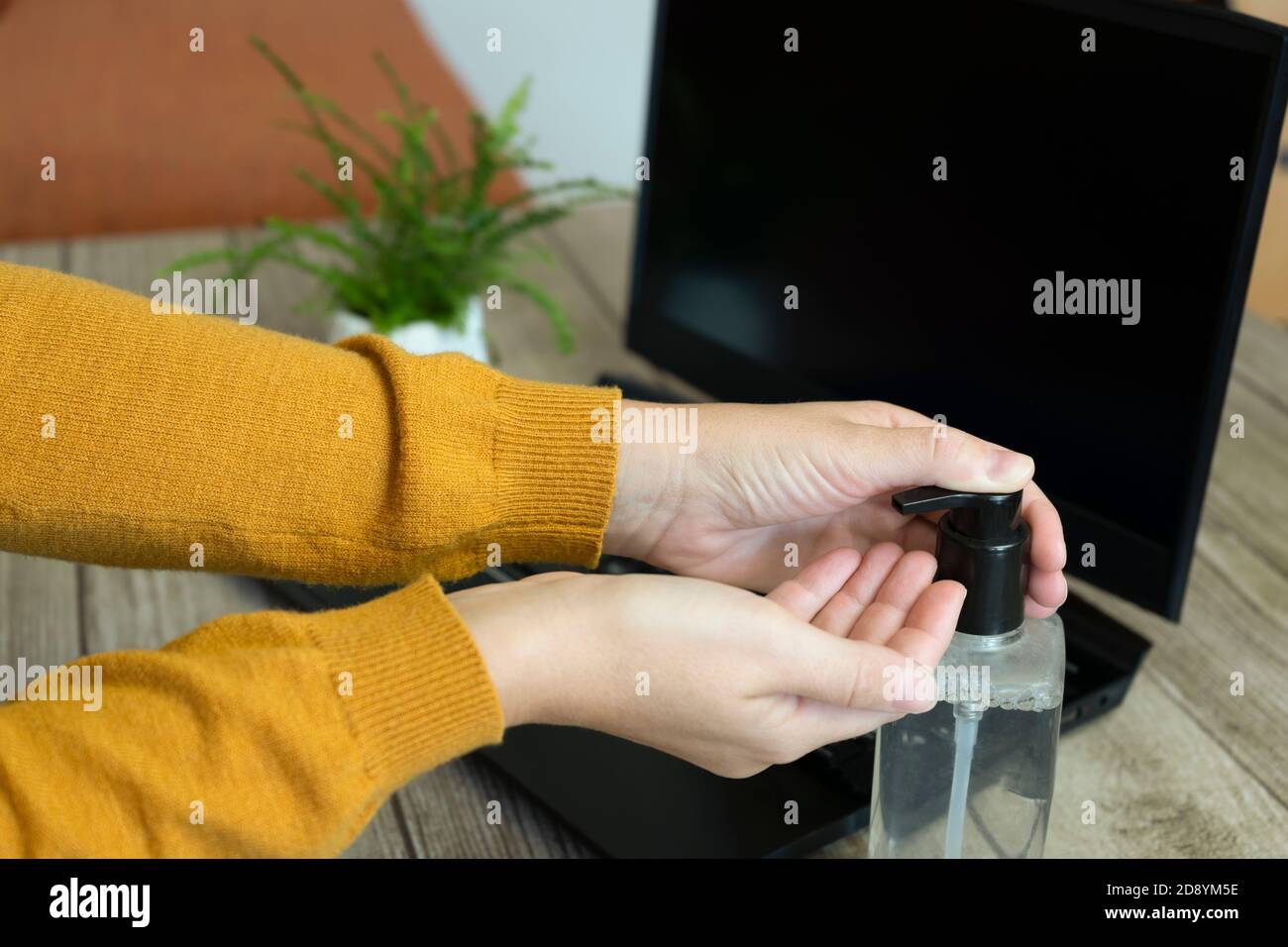 Femme appliquant de l'assainisseur pour les mains ou de l'hydrogel désinfectant les mains contre les germes, le coronavirus ou le covid-19, travaillant avec un ordinateur portable à la maison ou au bureau. Banque D'Images