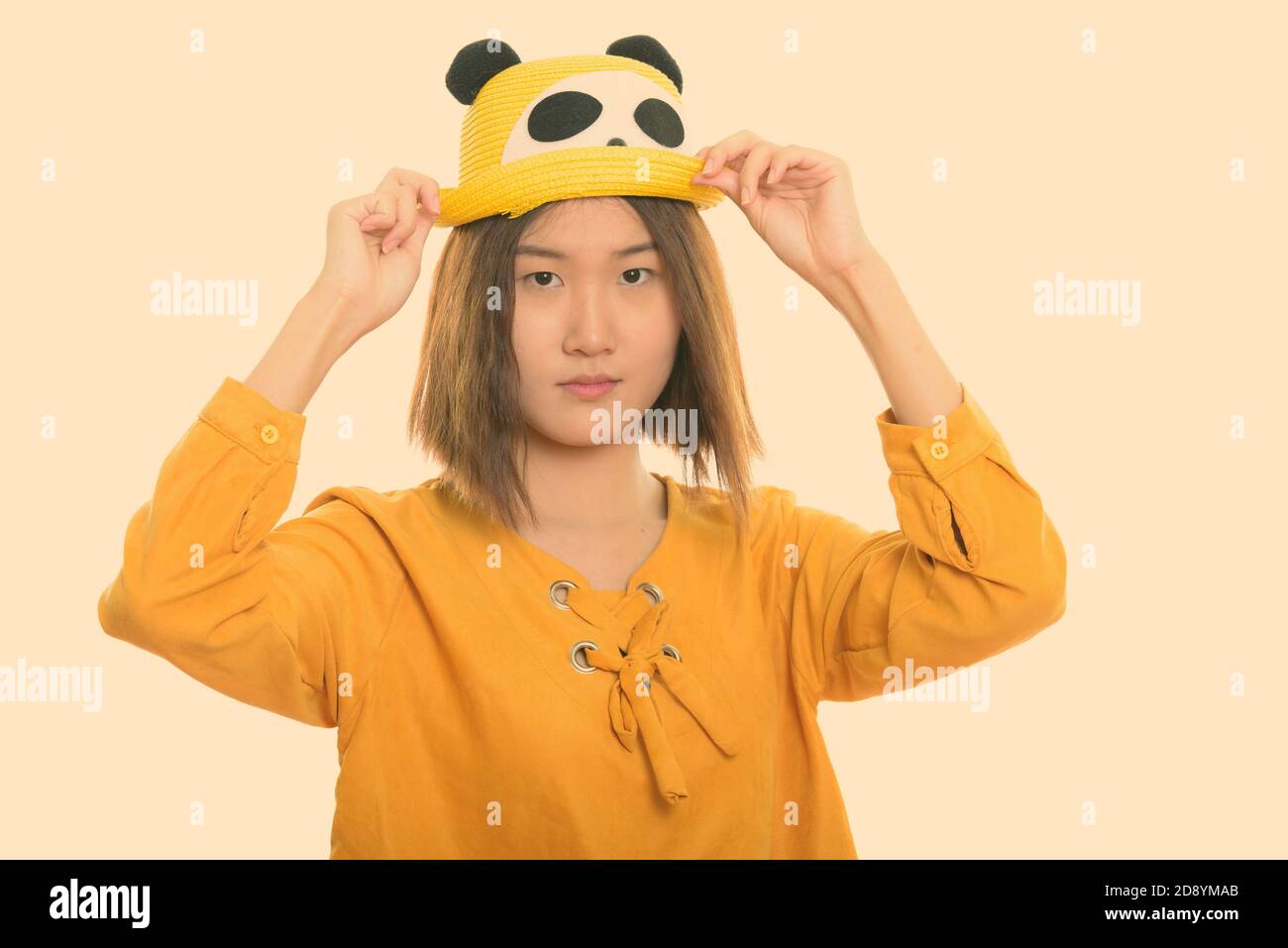Photo studio d'une jeune femme asiatique magnifique tenant un chapeau des deux mains Banque D'Images