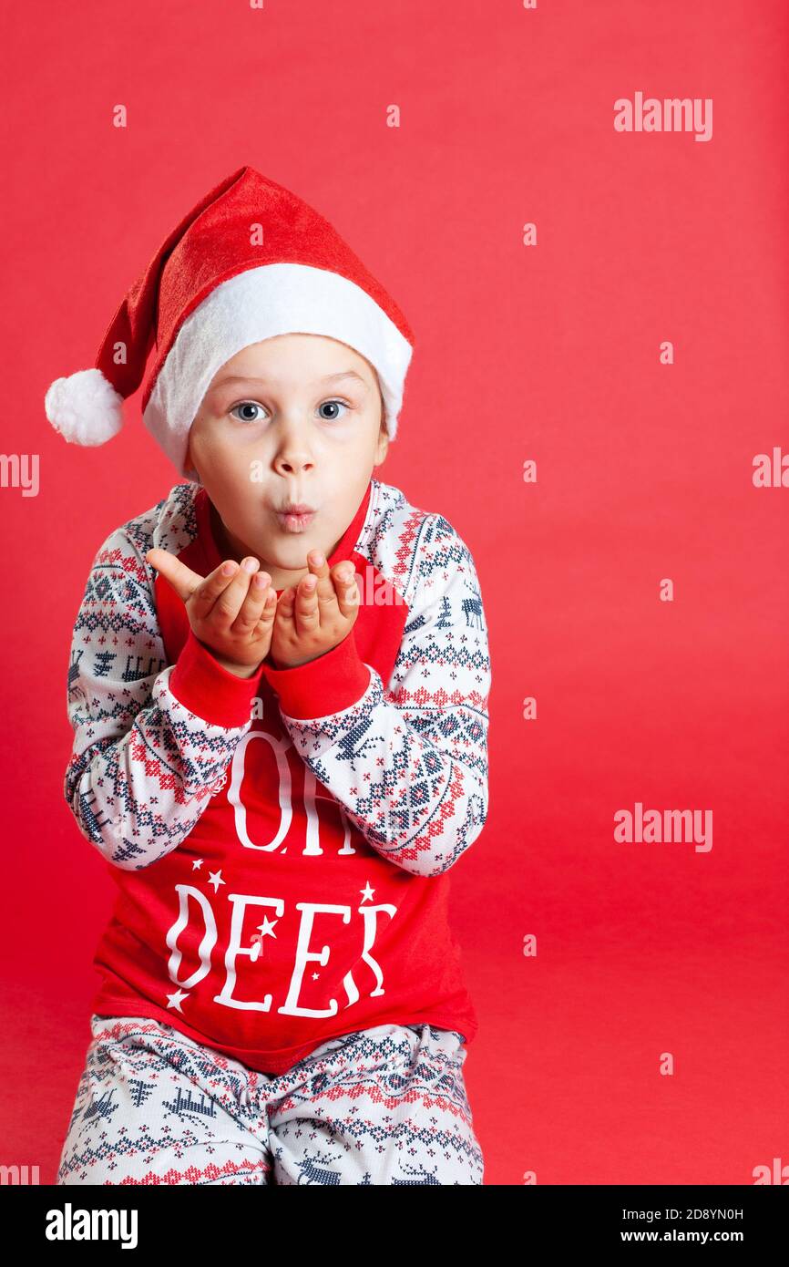 Gros plan fille en pyjama de Noël et chapeau de père Noël souffle un baiser, espace de copie sur un fond isolé vif Banque D'Images
