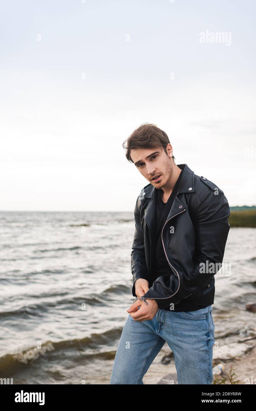 Jeune homme en Jean et veste en cuir regardant l'appareil photo sur la  plage Photo Stock - Alamy