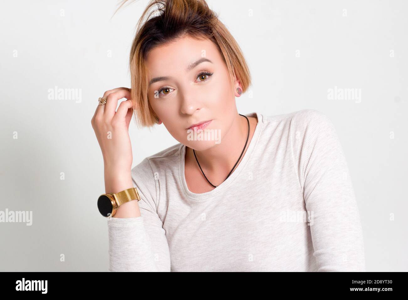 Portrait d'une jeune femme aux cheveux courts. Dans un chandail blanc et un pantalon vert. Sur fond blanc, il tient la tête dans ses mains Banque D'Images