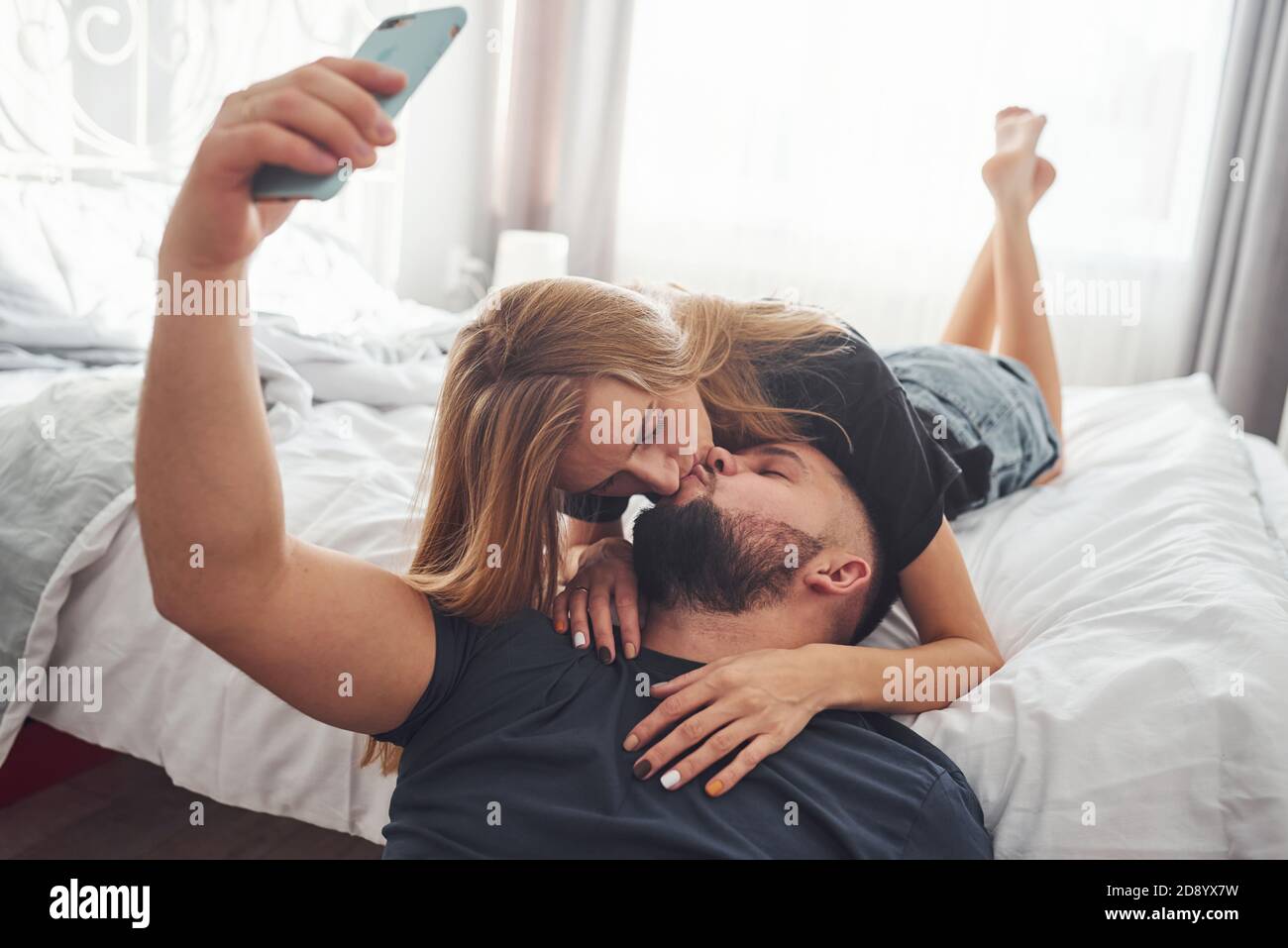 Jeune couple marié faisant un selfie en utilisant le téléphone dans chambre en journée Banque D'Images