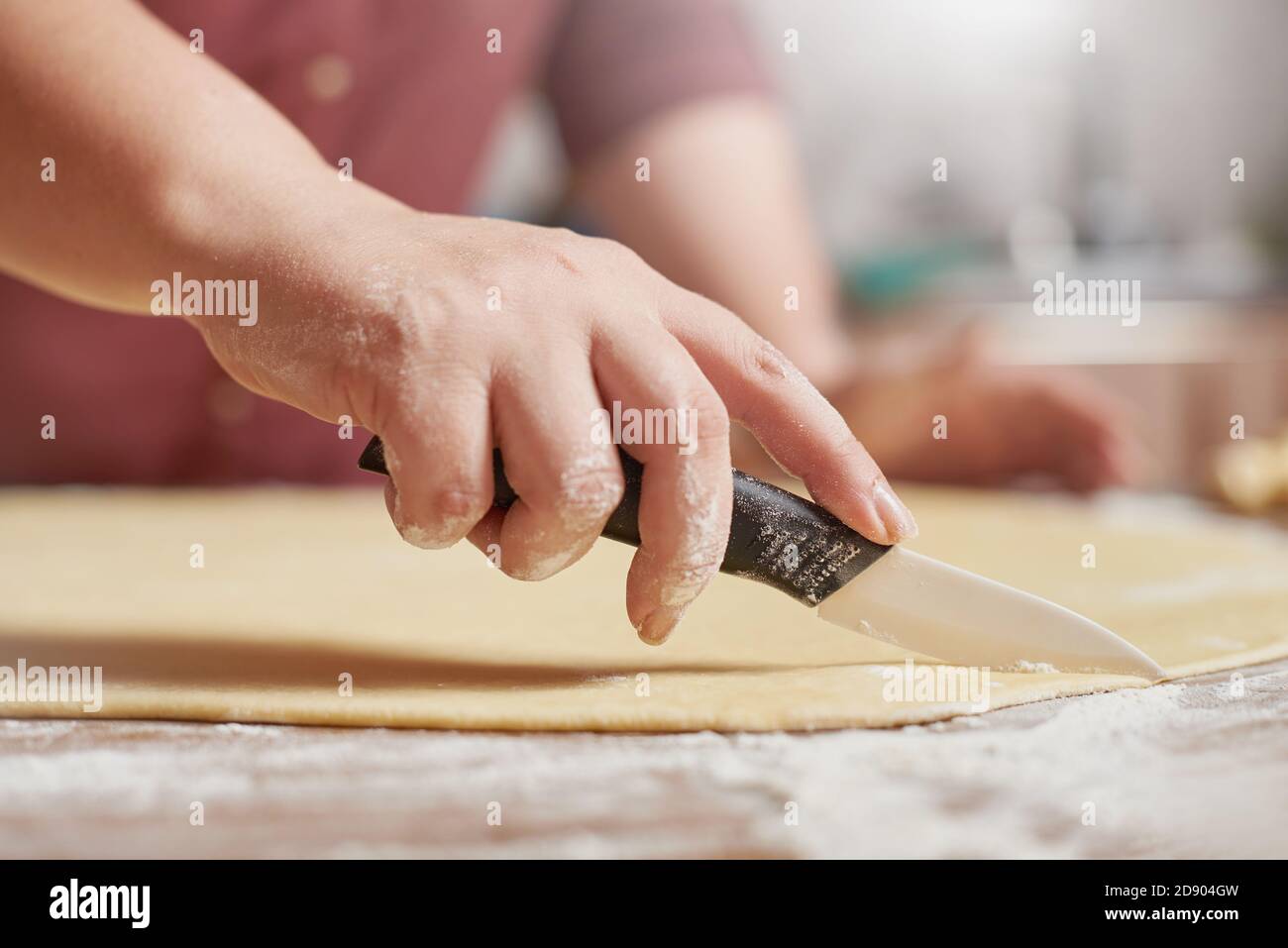 Gros plan des mains de femmes coupant la pâte crue avec un couteau Banque D'Images