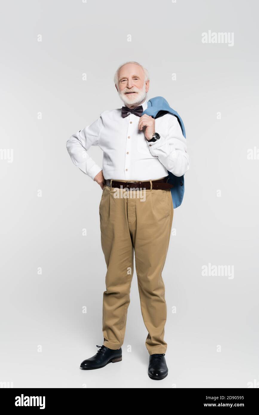 Homme senior souriant, main sur la hanche, tenant la veste arrière-plan gris Banque D'Images