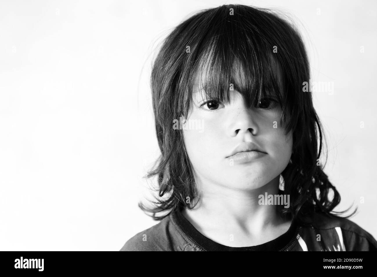 Portrait d'un garçon de 8 ans, avec de longs cheveux, tête et épaules tristes en noir et blanc. ©PRWPhotography Banque D'Images